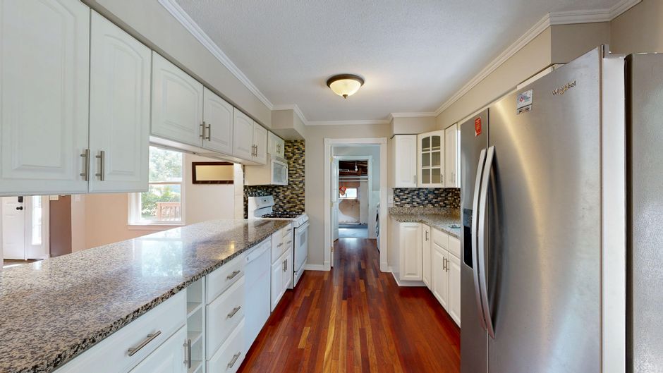 Spacious modern kitchen featuring granite countertops, stainless steel fridge, and wooden flooring.